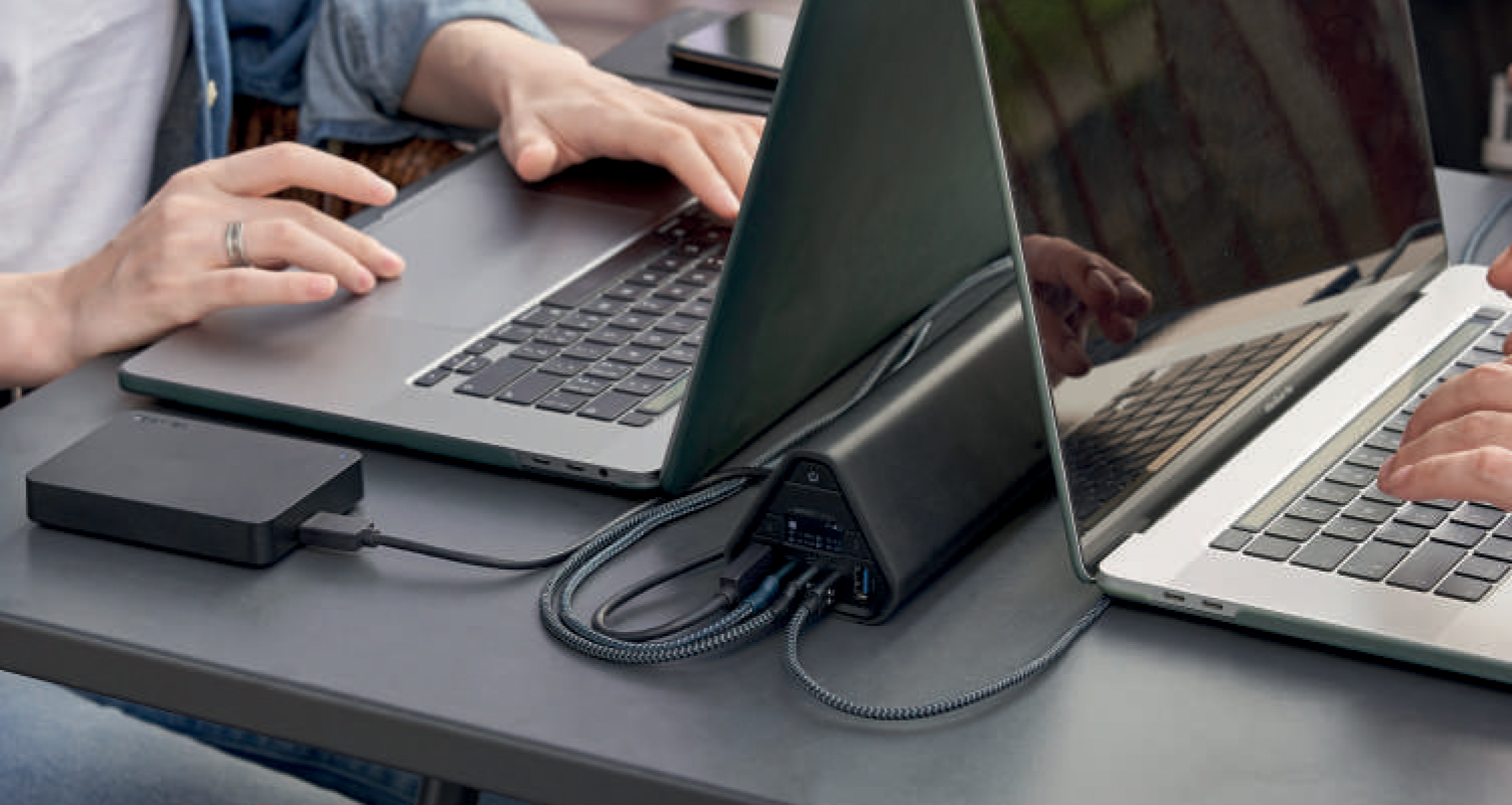 omnicharge portable charger connected two to laptops with hands typing on one of the laptop keyboards